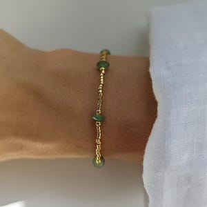 Peut inclure: Un bracelet délicat composé d'une série de petites perles cylindriques dorées métalliques entrecoupées de trois perles vertes translucides à facettes. Le design est simple et linéaire, présentant un motif répétitif d'éléments dorés et verts.