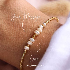 Peut inclure: Un bracelet délicat composé d'un motif alternant de petites perles cylindriques en métal doré et de perles d'eau douce blanches irrégulières. L'image comporte le texte Your Message avec une flèche et le mot Love inscrit en dessous.