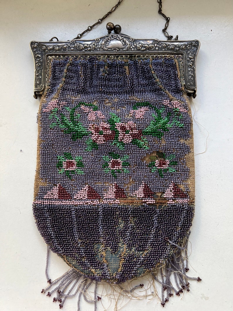 May include: A vintage beaded purse with a silver clasp and chain. The purse is decorated with a floral design in shades of pink, green, and purple.
