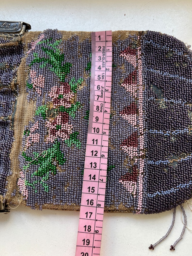May include: A beaded purse with a floral design in shades of pink, green, and purple. The purse is approximately 17 inches long and has a silver clasp.