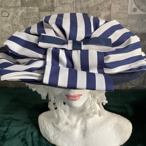 May include: A blue and white striped sun hat with a large bow. The hat is displayed on a white bust. The hat's brim is dark blue.