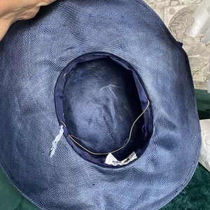 May include: A navy blue sun hat with a wide brim. The hat features a striped ribbon and a dark blue interior lining. The hat is made of woven material and has a tag inside.