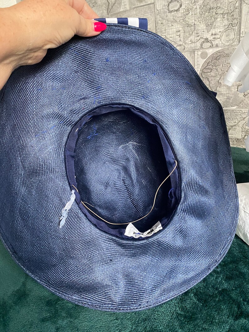 May include: A navy blue sun hat with a wide brim. The hat features a striped ribbon and a dark blue interior lining. The hat is made of woven material and has a tag inside.