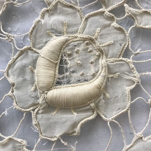 May include: Close-up of a delicate white crocheted lace doily with a floral design. The lace is intricate and detailed, with a central flower motif.