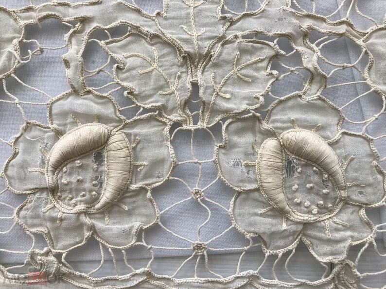 May include: Close-up of a delicate white lace fabric with intricate floral designs. The fabric features a repeating pattern of flowers with raised centers and a fine mesh background.