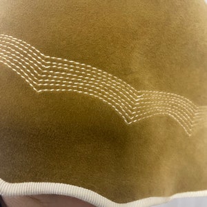 May include: A brown velvet bucket hat with a white stitched design around the brim. The hat has a white trim around the edge.