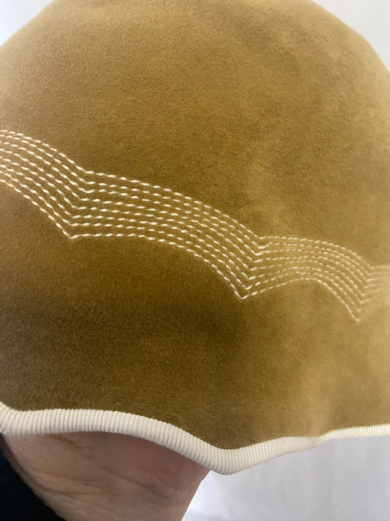 May include: A brown velvet bucket hat with a white stitched design around the brim. The hat has a white trim around the edge.