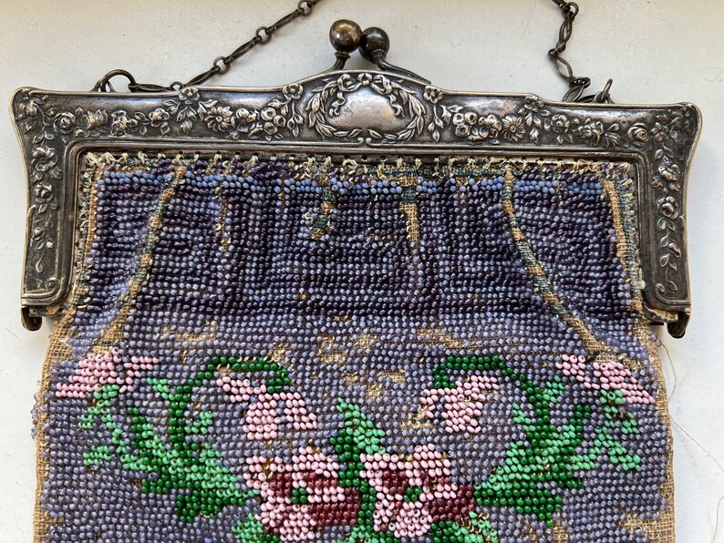 May include: A vintage beaded purse with a silver frame and floral design. The purse is made of small, colorful beads and features a floral pattern with pink, green, and purple beads.