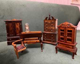 May include: A collection of miniature wooden furniture including a tall wardrobe, a desk with a small glass dome, a chest of drawers with a decorative top, a glass-fronted cabinet, and a small chair with a patterned seat cushion.