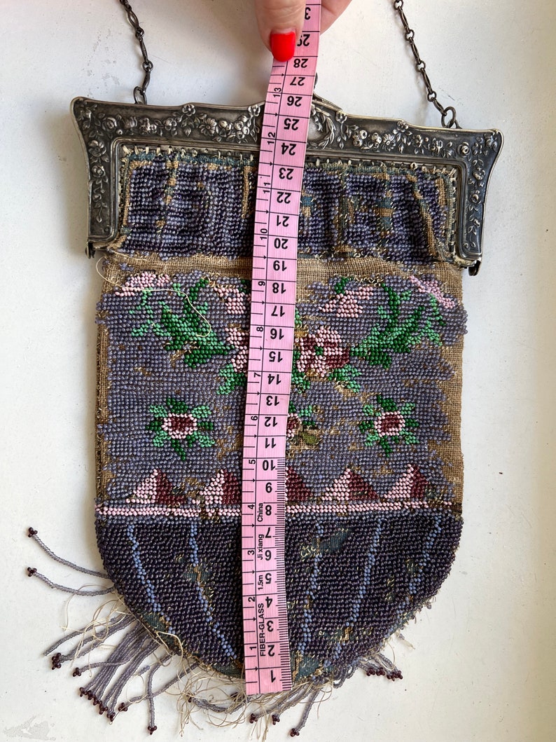 May include: A beaded purse with a silver frame and a chain strap. The purse is decorated with floral designs in shades of pink, green, and purple. The purse measures approximately 28 inches in length.