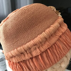 May include: A peach-colored hat with a ruffled brim. The hat is made of a soft, textured fabric.