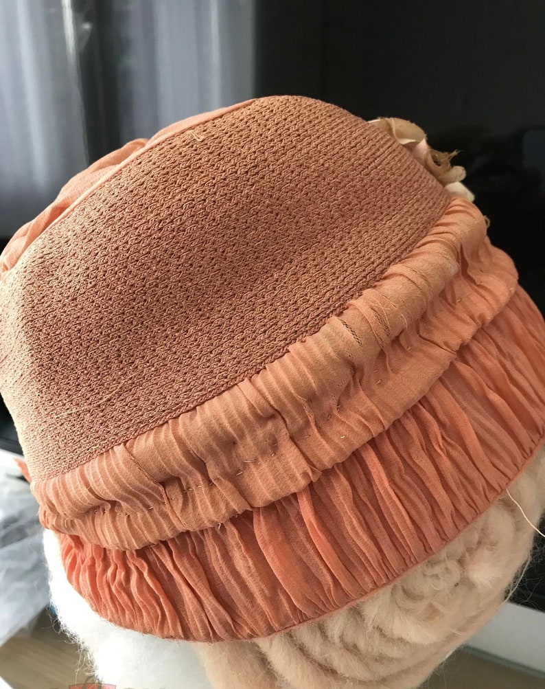 May include: A peach-colored hat with a ruffled brim. The hat is made of a soft, textured fabric.