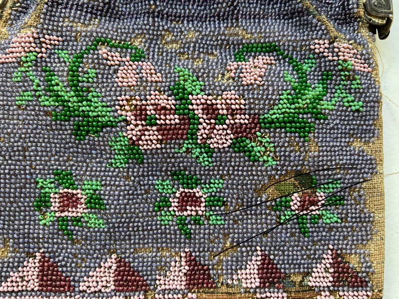 May include: A vintage beaded purse with a floral design. The purse is made of small, colorful beads in shades of pink, green, and brown, sewn onto a light purple fabric. The purse has a clasp closure and a beaded fringe.