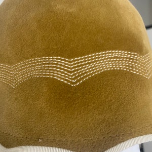 May include: A brown felt hat with a white stitched design around the brim. The hat has a white trim around the edge.