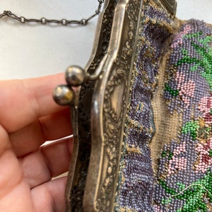 May include: A vintage beaded purse with a silver frame and a chain strap. The purse is decorated with a floral pattern in shades of purple, pink, and green.