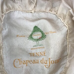 May include: A white hat with a green pine tree logo and the text "Paris Creators New York Registered TENN&Eacute; Chapeau du Jour".