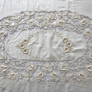 May include: A white oval tablecloth with a delicate lace border and embroidered floral designs.