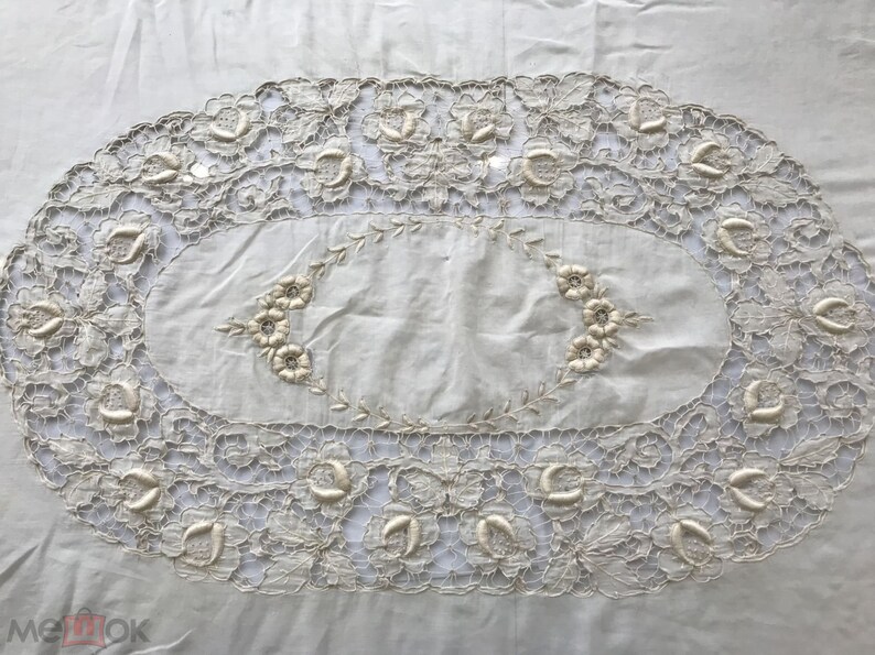 May include: A white oval tablecloth with a delicate lace border and embroidered floral designs.