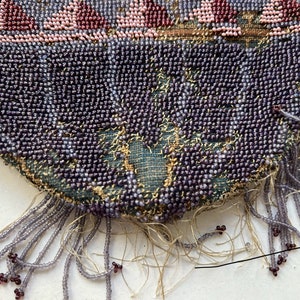 May include: A close-up of a beaded purse with a fringe of purple beads. The purse is made of a dark green fabric with a floral pattern.