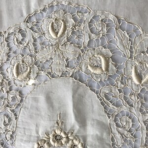 May include: A white cotton tablecloth with delicate embroidered floral designs. The embroidery is in a cream color and features intricate patterns of leaves and flowers.