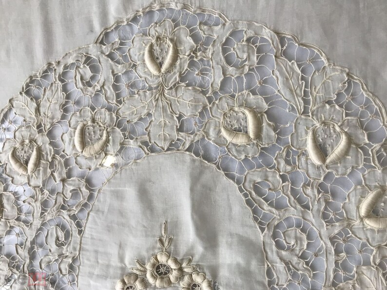 May include: A white cotton tablecloth with delicate embroidered floral designs. The embroidery is in a cream color and features intricate patterns of leaves and flowers.