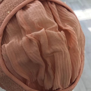 May include: A close-up of the inside of a light brown straw hat with a light pink fabric lining. The fabric is gathered and pleated.