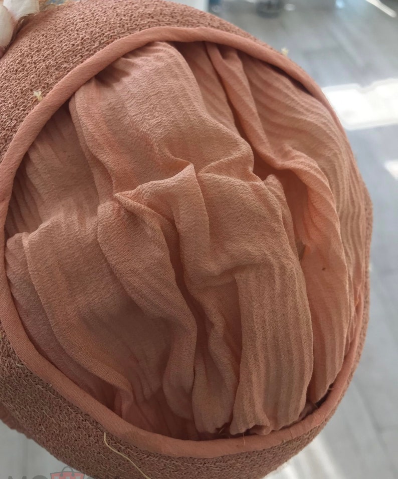 May include: A close-up of the inside of a light brown straw hat with a light pink fabric lining. The fabric is gathered and pleated.