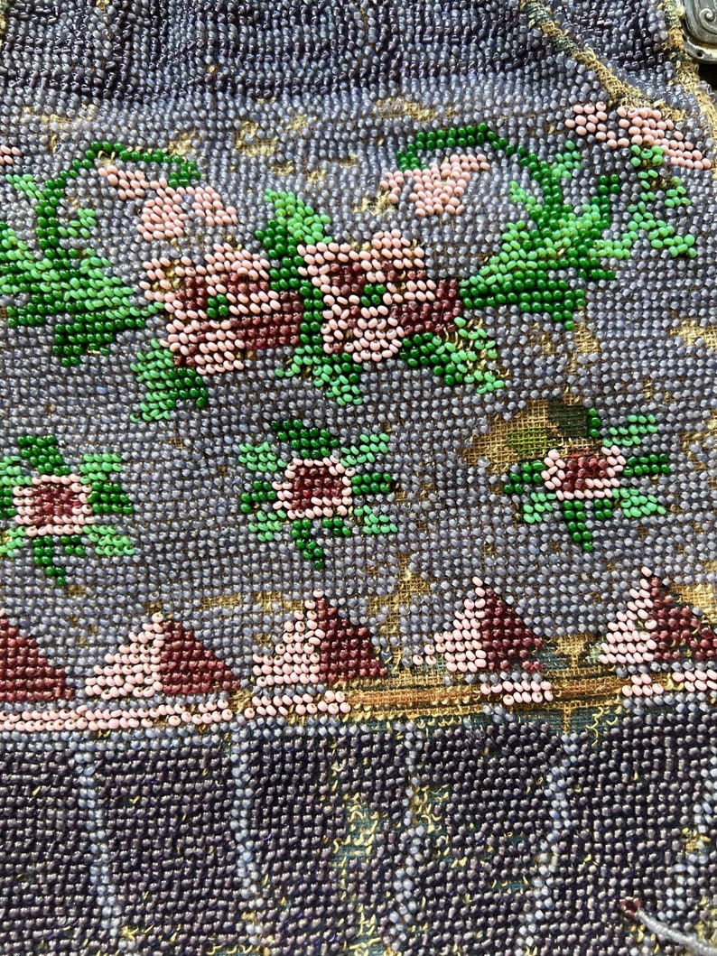 May include: Close-up of a beaded purse with a floral design. The purse is made of small, iridescent beads in shades of blue, green, pink, and brown. The floral design is intricate and detailed, with leaves and flowers.