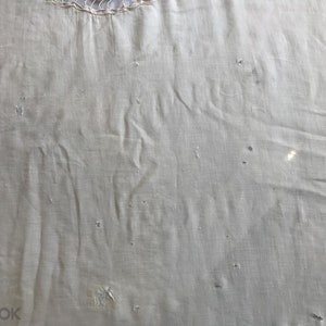 May include: A close-up of a plain, off-white fabric with a few small holes. The fabric has a slightly textured surface.