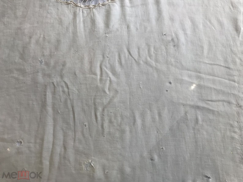 May include: A close-up of a plain, off-white fabric with a few small holes. The fabric has a slightly textured surface.