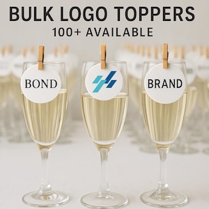 May include: Three champagne flutes with white circular toppers clipped on with wooden pegs. The toppers have the words "BOND" and "BRAND" printed on them, and one has a blue and teal logo. The text "BULK LOGO TOPPERS" and "100+ AVAILABLE" are at the top.