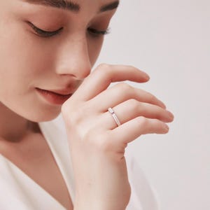 Puede incluir: Un fino anillo de banda de plata con una pequeña piedra preciosa rosa engastada en el centro.