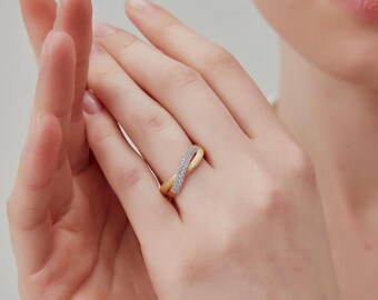 May include: A gold-toned ring with an infinity symbol design. One side of the ring is encrusted with small, sparkling white stones. The ring is worn on a finger, with the hands in the foreground.