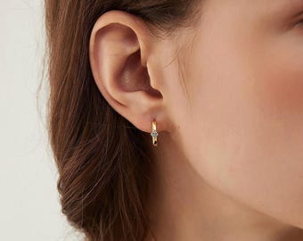 Puede incluir: Primer plano de una oreja con un pequeño aro de oro con una sola piedra transparente.