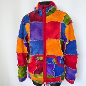 Puede incluir: Chaqueta de patchwork colorida con cremallera y capucha rojas. La chaqueta presenta una variedad de colores, incluyendo rojo, naranja, azul, verde y morado. Los bordes de los parches tienen una costura ondulada decorativa.