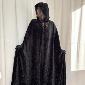 May include: A black hooded cape with a textured, fuzzy fabric. The cape is long and flowing, with a hood that can be pulled up over the head.