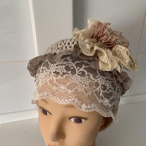 May include: A white crocheted hat with a brown crocheted band and a large beige and pink flower accent.