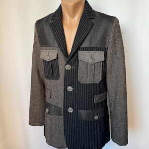 May include: A two-tone blazer with a unique design. The jacket features a combination of gray herringbone and black pinstripe fabrics. It has four front pockets, a notched lapel, and button closures. The blazer is displayed on a mannequin.