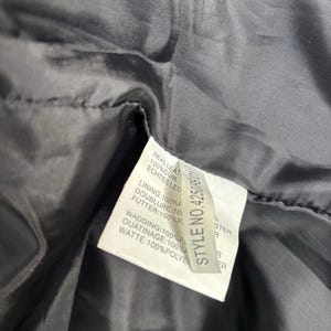 May include: Close-up of a black garment's interior, revealing a tag with text in multiple languages. The tag lists the materials: real leather, lining, wadding, and other components. The style number is 42500.