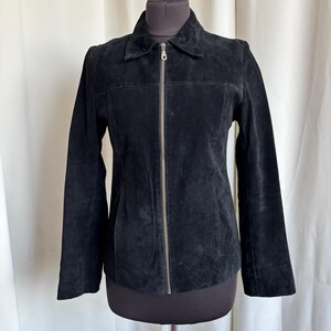 May include: A black suede jacket with a collared neckline and a full-length zipper closure. The jacket is displayed on a mannequin and has long sleeves. The suede material has a soft, textured appearance.