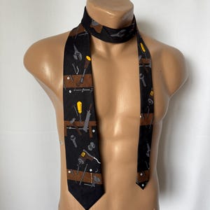 May include: A black necktie featuring a pattern of various tools, including a saw, hammer, screwdriver, and wrench. The tools are depicted in shades of brown, grey, and yellow.