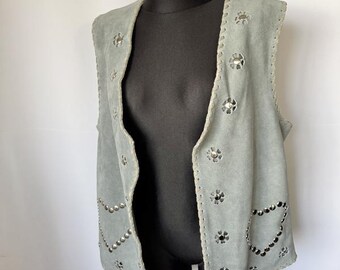 May include: A light blue suede vest with decorative silver studs and cut-out floral designs. The vest has a sleeveless design and a cream-colored stitched trim. The vest is displayed on a black mannequin.