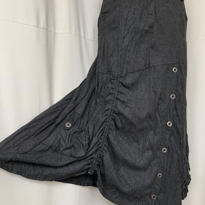 May include: A dark gray long skirt with a gathered detail on the side and multiple button accents.