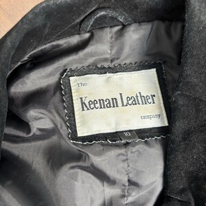 May include: Close-up of a black leather jacket's interior. The lining is black, and a label reads "The Keenan Leather company." The label is white with black text and a decorative border. A size 10 tag is visible.