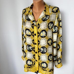 May include: A patterned long-sleeved shirt. The shirt has a cream background with yellow and black geometric shapes and floral accents. The collar and cuffs are trimmed in yellow. The shirt is buttoned down the front.