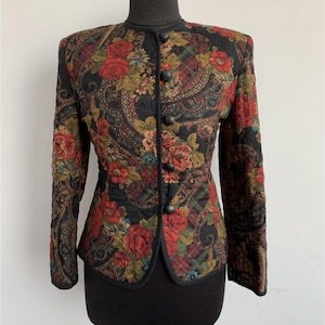 Op de afbeelding: Een zwart gewatteerd jack met een bloemen-paisley print. Het jack heeft een mandarijnkraag, een knoopsluiting en lange mouwen.