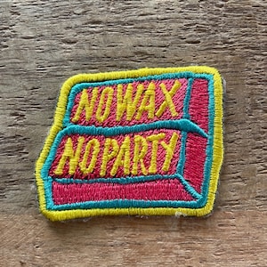 Può includere: Una toppa ricamata rosa e gialla con il testo "No Wax No Party" su uno sfondo di legno.