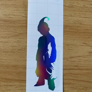 May include: A holographic vinyl sticker featuring a silhouette of a character from the Dragon Ball Z anime series. The sticker has a gradient of colors, including green, yellow, blue, and purple. The character is in a standing pose.