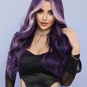 May include: A woman with long, wavy purple hair with a light purple highlight. She is wearing a black top, a silver necklace, and blue jeans. The background is a light blue.
