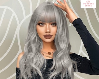 May include: A silver-gray wig with long, wavy hair and a blunt fringe. The wig features a natural-looking hairline and is styled with loose waves. The image also shows a black top and a gold necklace. The Wig Wonders Store logo is visible in the top right corner.